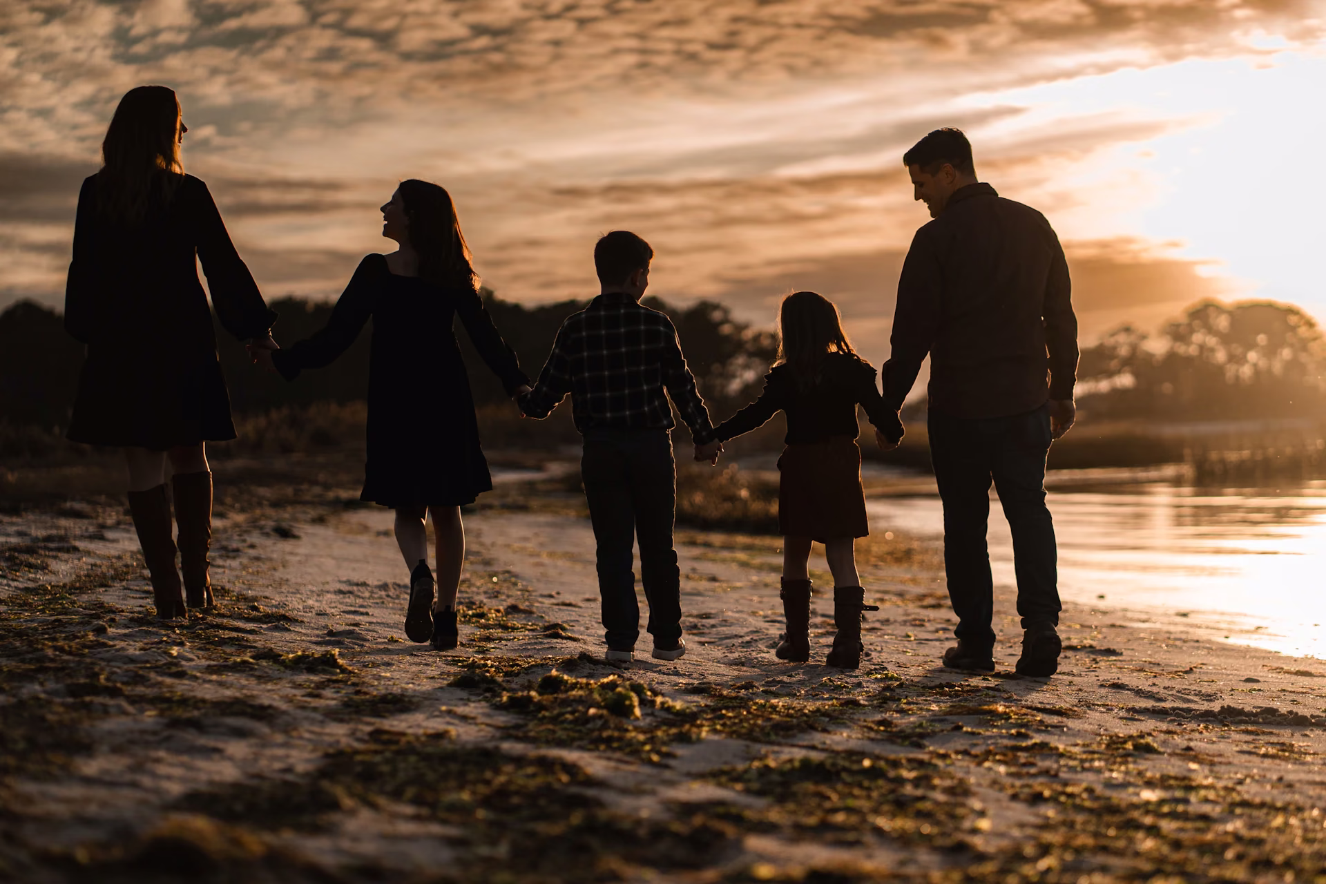 Família de mãos dadas caminhando na praia ao pôr do sol